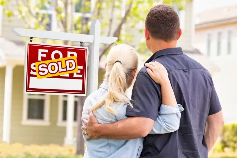 a millennial couple facing the front of sold house