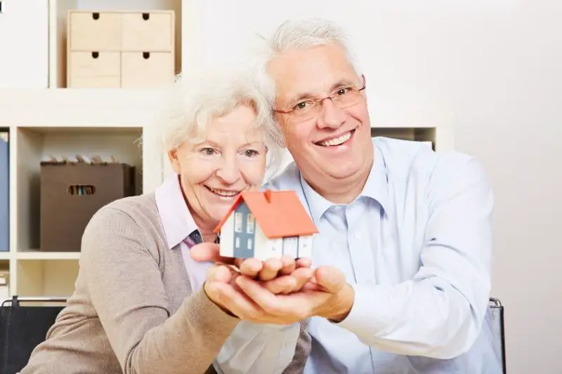 happy senior couple holding a small house