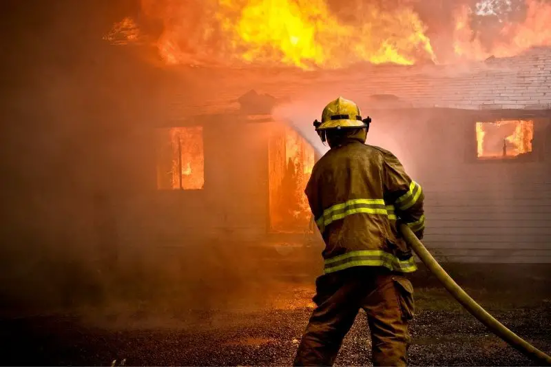 firefighter spraying water at a house fire