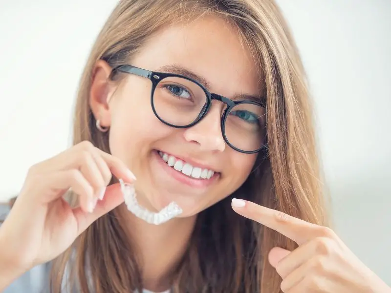 a girl smiling and holding dental invisible braces for invisalign