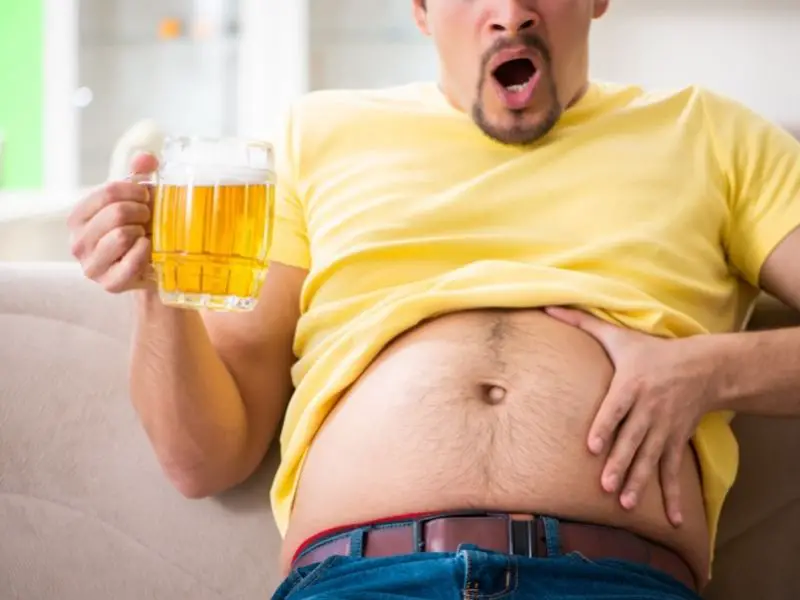 man holding a glass of beer and staring at his beer belly