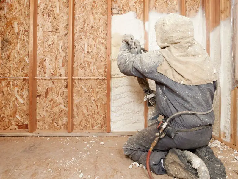 worker spraying foam insulation between wall studs
